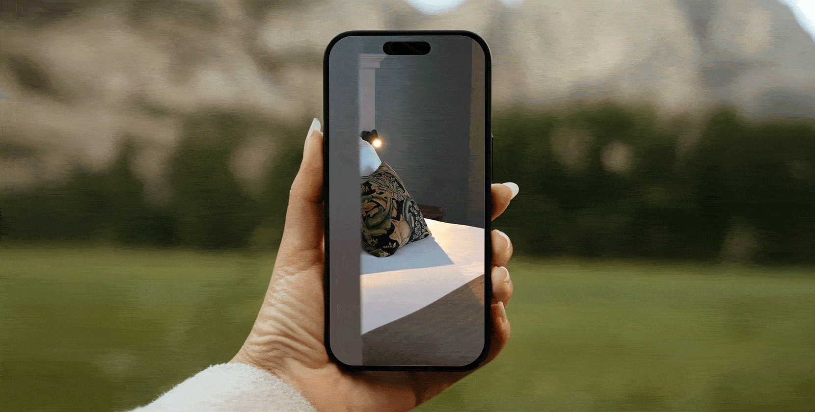 A hand holding a phone with a hotel room on the screen.