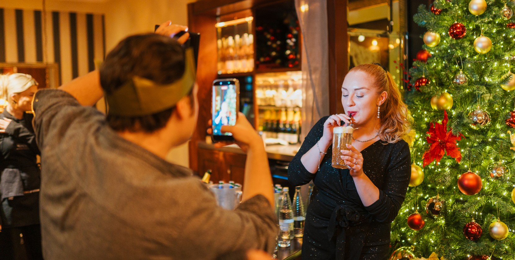 Content creators record festive drinks content on a smartphone in front of a luxury Christmas tree.