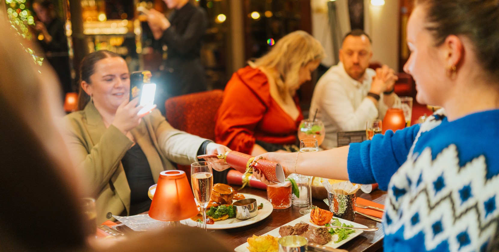 Social media content creators film themselves pull a Miller and Carter Christmas cracker over a festive dinner table.