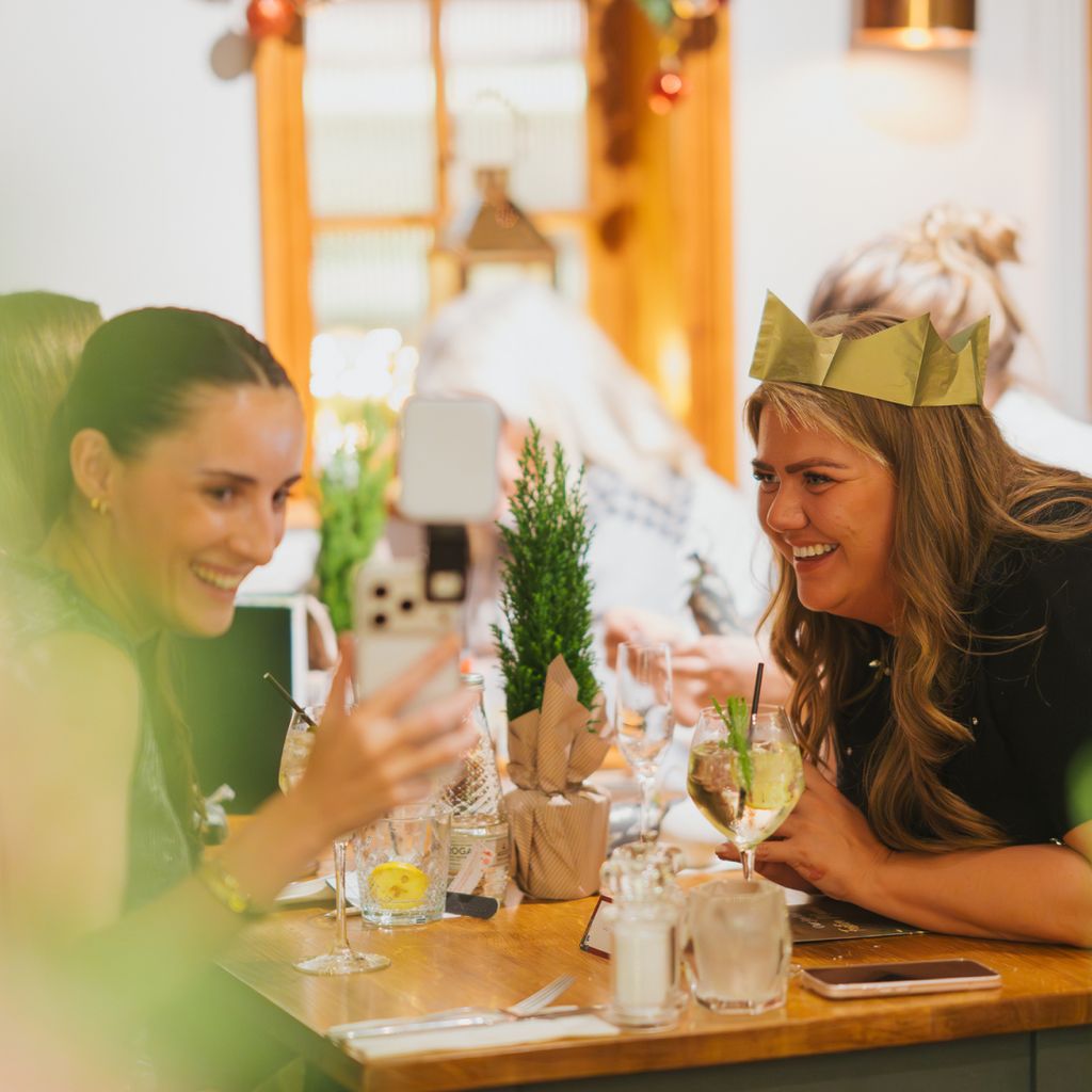 Two social media content creators look at a smartphone over a festive dinner table.
